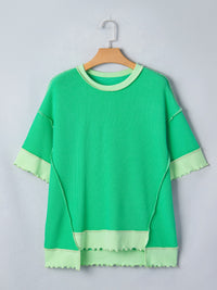 Green textured top with ruffled edges on a hanger against a light gray background