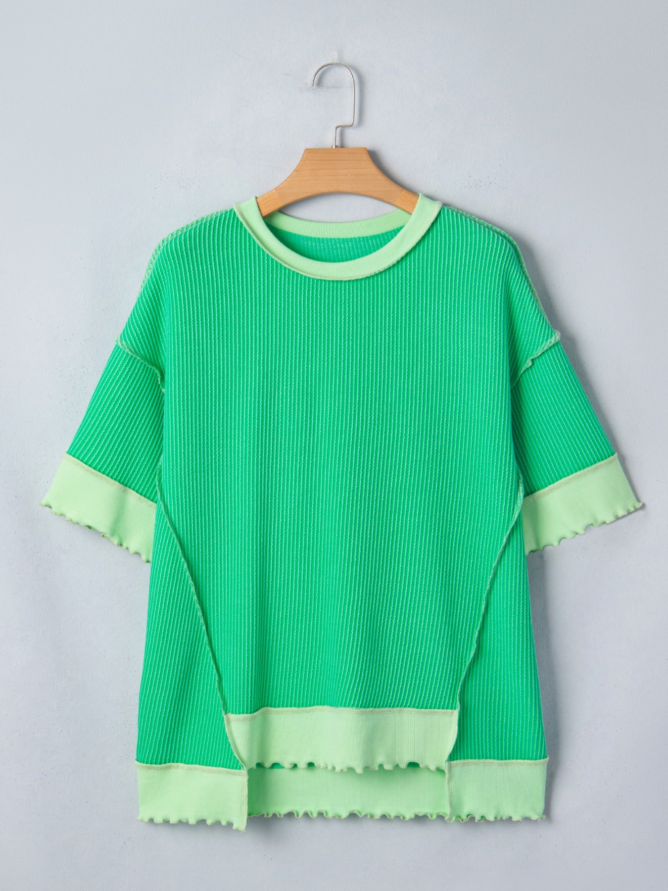 Green textured top with ruffled edges on a hanger against a light gray background
