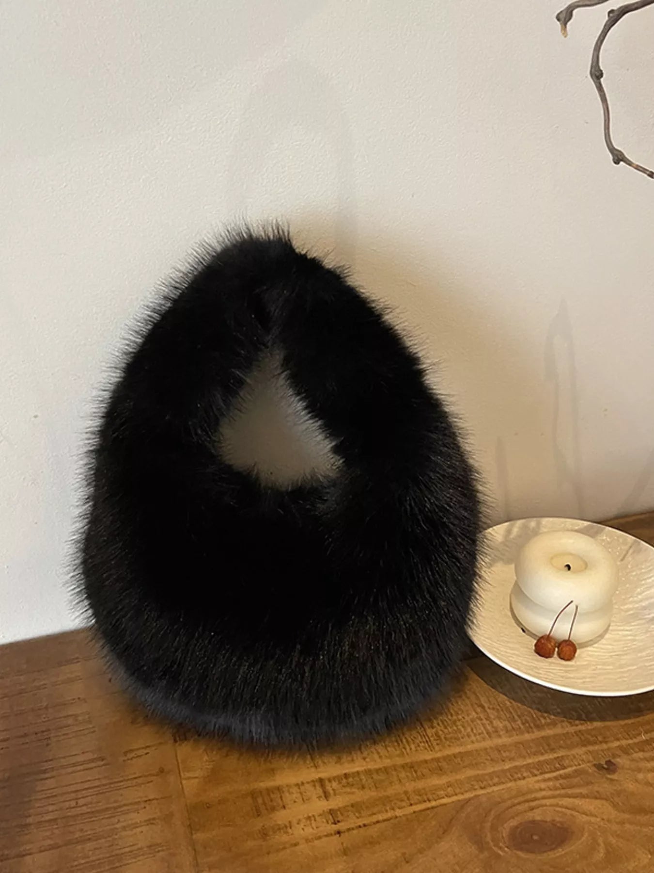 Black fur collar on a wooden surface with a white wall and decorative items in the background.