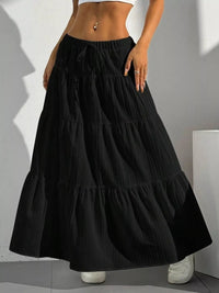 Black tiered skirt worn by a person against a neutral background