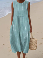 Woman in a light blue dress holding a straw bag on a beach.