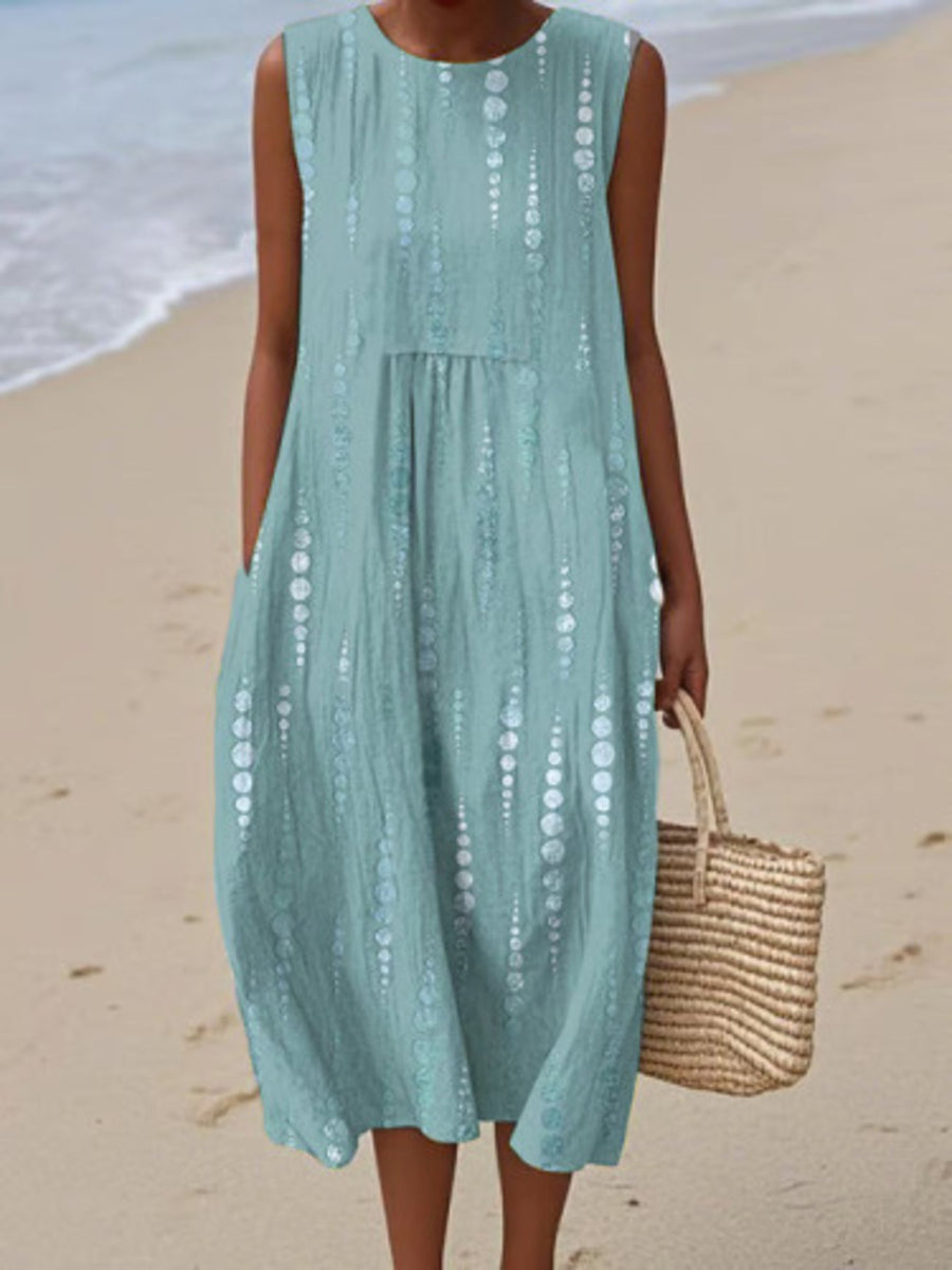 Woman in a light blue dress holding a straw bag on a beach.