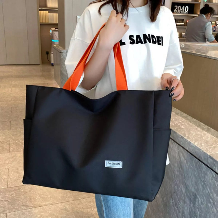 Person holding a black tote bag with orange handles in an indoor setting
