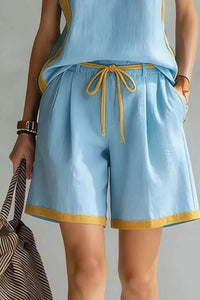 Light blue sleeveless top and shorts with yellow trim, held by a person against a neutral background.