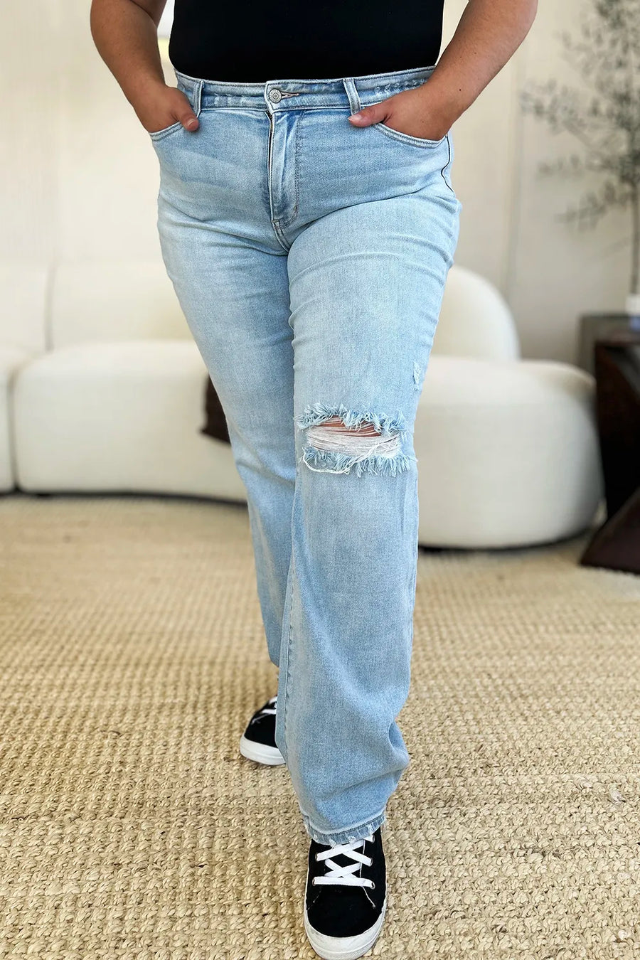 Person wearing light blue jeans with a slight distressed look, standing on a carpeted floor.