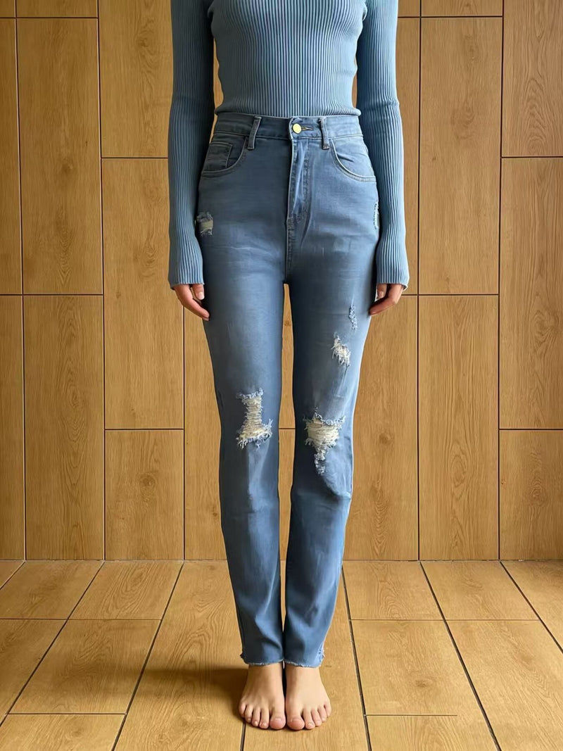 Person wearing a blue ribbed long-sleeve top and distressed blue jeans standing against a wooden paneled wall.
