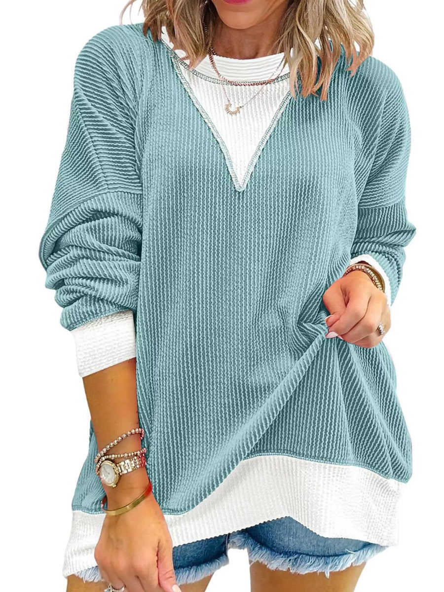 Woman wearing a light blue sweater over a white shirt with denim shorts on a white background