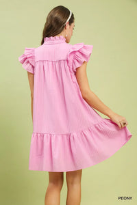 Pink dress with ruffled sleeves and bottom on a green background