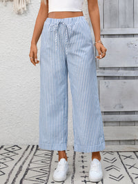 Person wearing blue and white striped wide-leg pants with a white top and white sneakers, standing on a patterned rug.
