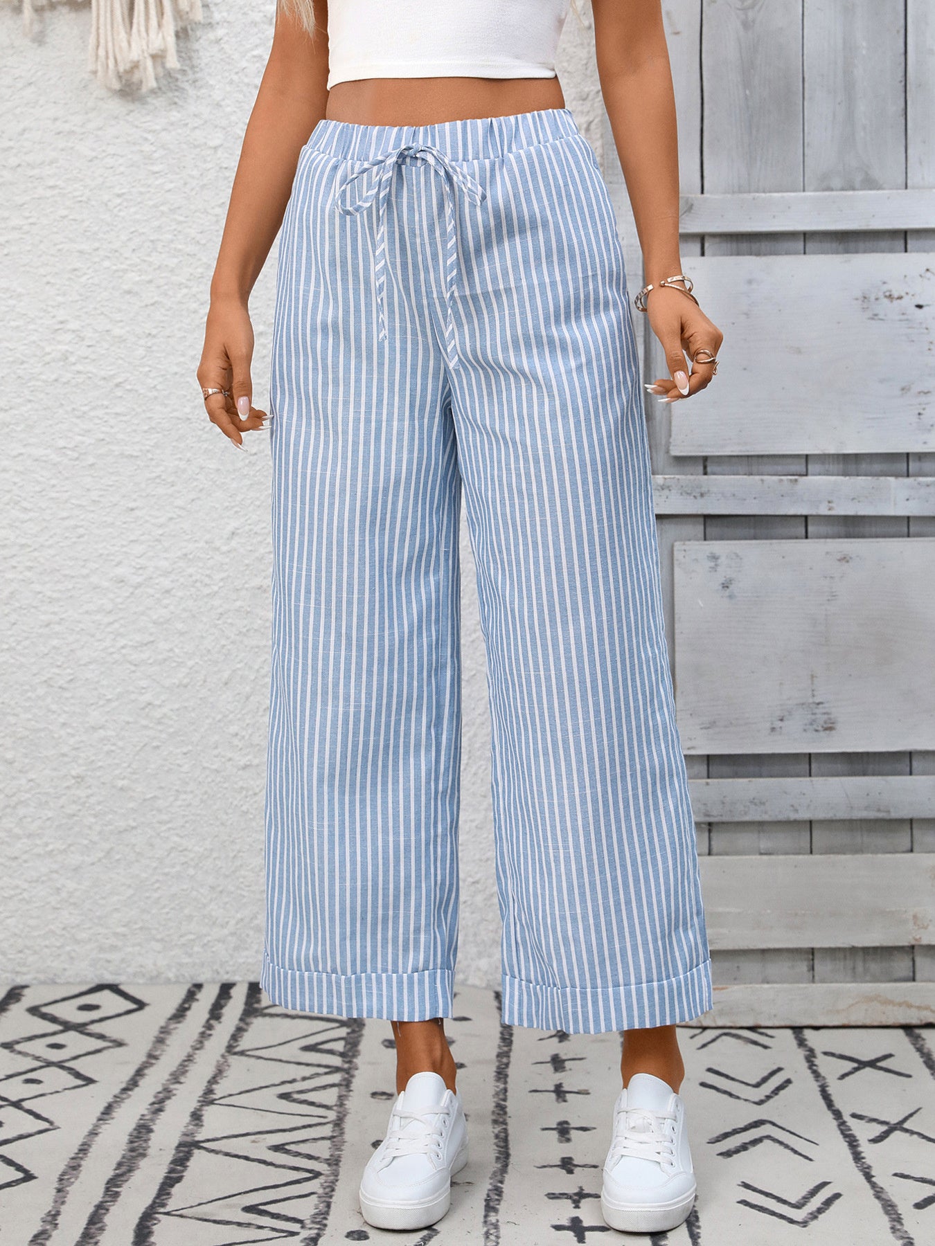 Person wearing blue and white striped wide-leg pants with a white top and white sneakers, standing on a patterned rug.