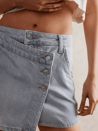 Light blue denim skirt with button details on a neutral background