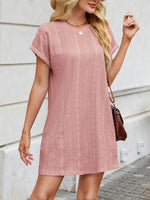 Woman wearing a pink lace dress standing against a light-colored wall.