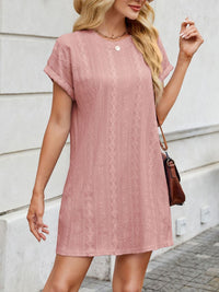 Woman wearing a pink lace dress standing against a light-colored wall.