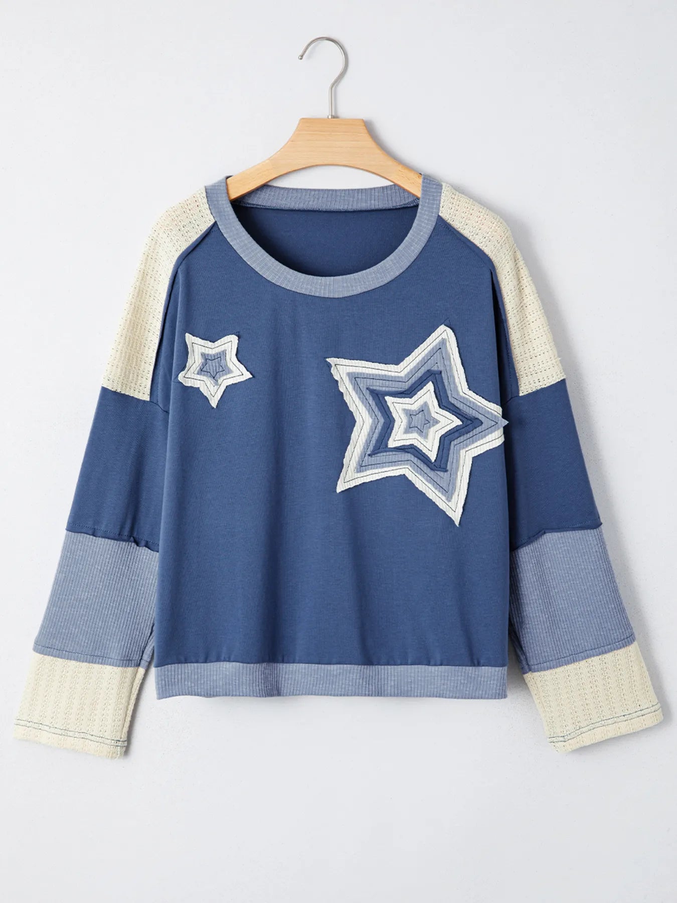 Blue sweater with star designs on a hanger against a white background
