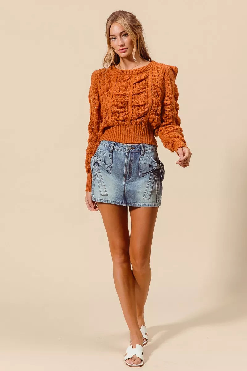 Woman wearing an orange cable knit sweater and denim skirt on a beige background