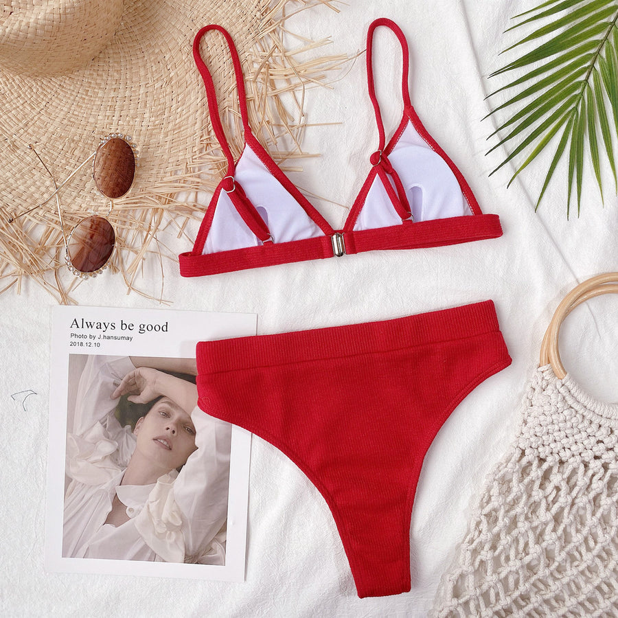 Red bikini set on a textured surface with a magazine and natural elements.
