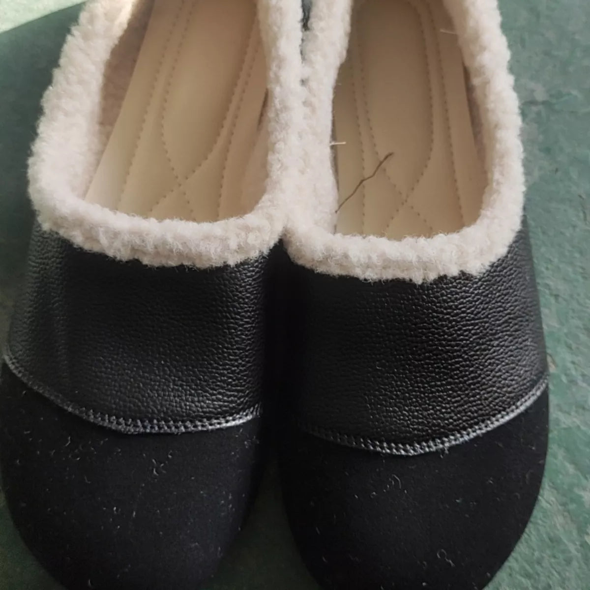 Pair of black slippers with white lining on a green surface
