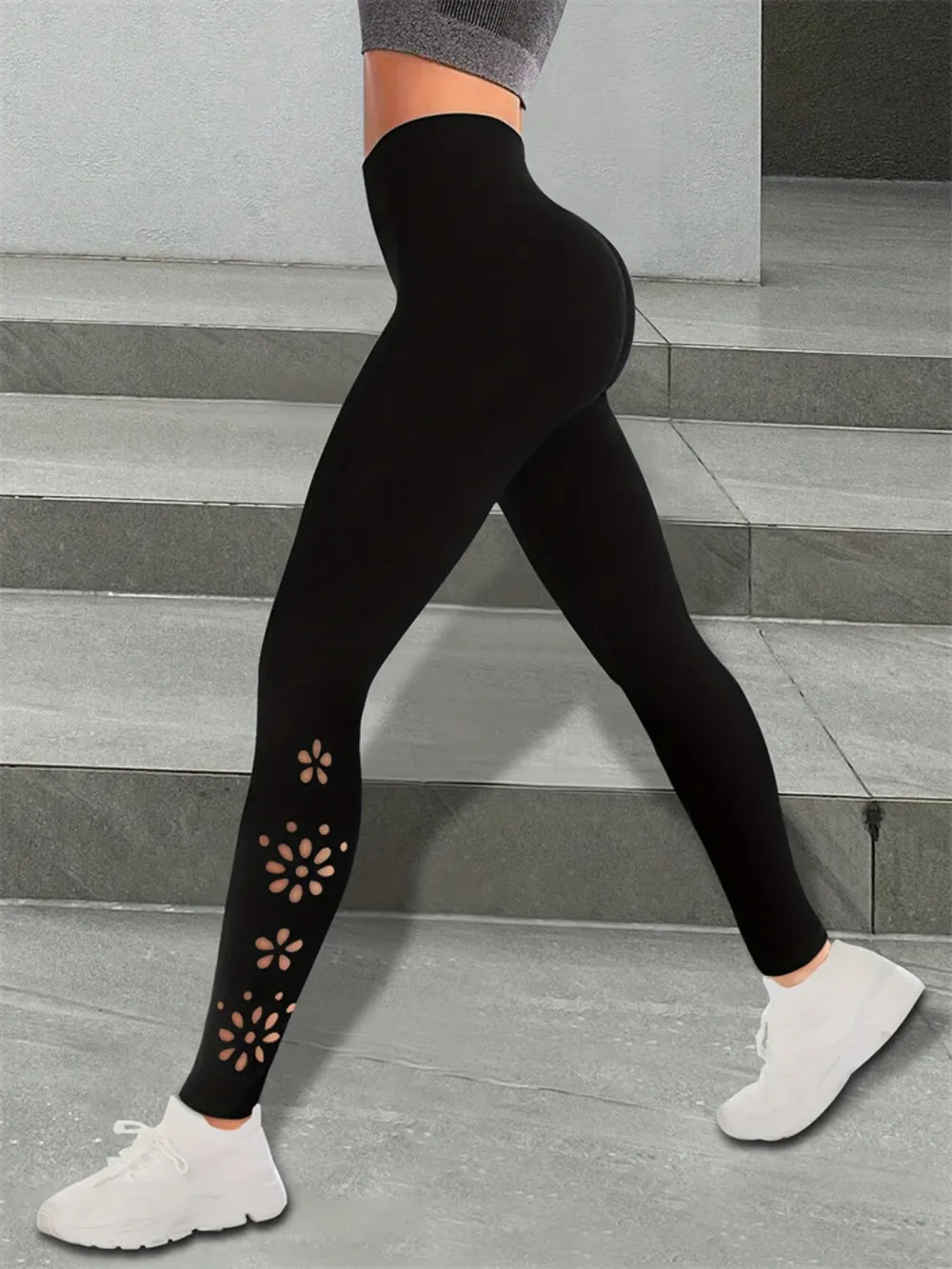 Person wearing black leggings with floral cutouts on a concrete surface.