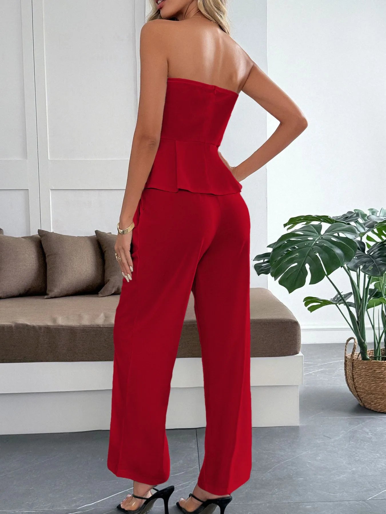 Woman wearing a red strapless jumpsuit in a modern living room.