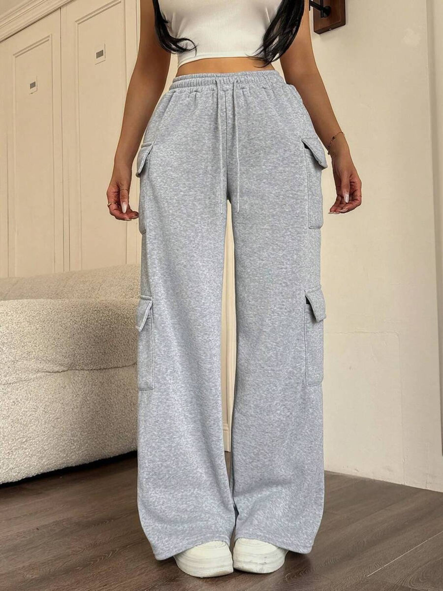 Person wearing gray wide-leg pants with pockets in a room.