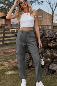 Woman wearing a white crop top and gray cargo pants standing in front of a stone wall.