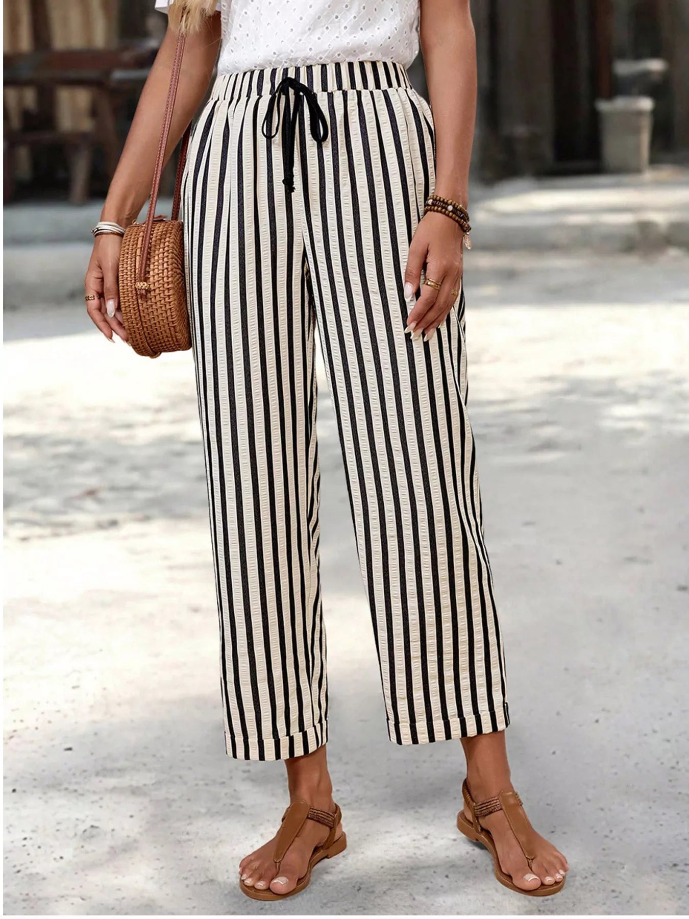 Person wearing black and white striped pants with a woven bag on a blurred street background
