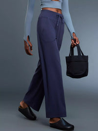 Person wearing navy pants and a light blue top, holding a black tote bag on a gray background