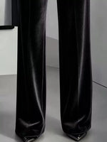 Black wide-leg trousers with a satin or velvet-like sheen, shown from the knees down on a model wearing pointed metallic heels.
