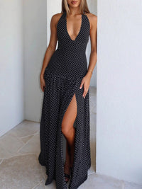 Woman wearing a black and white polka dot dress with a deep neckline and high slit in a minimalistic setting.