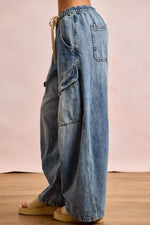 Blue jeans worn by a person on a wooden floor with a pinkish-beige background