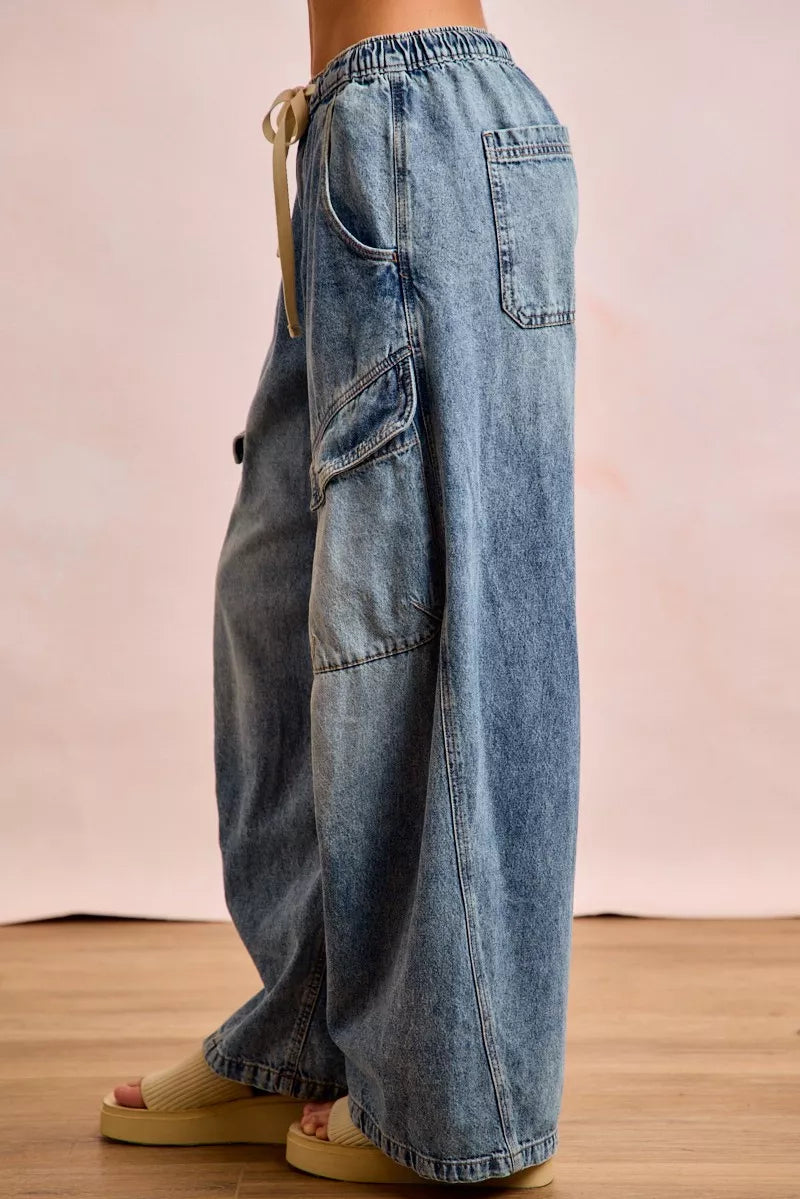 Blue jeans worn by a person on a wooden floor with a pinkish-beige background