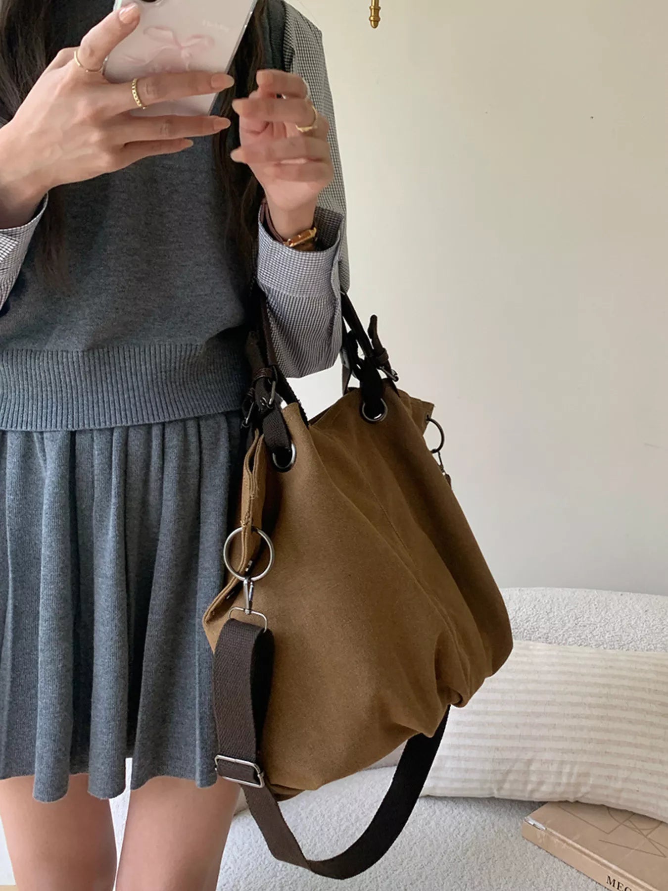 Person wearing a gray sweater and skirt with a brown handbag, taking a mirror selfie.
