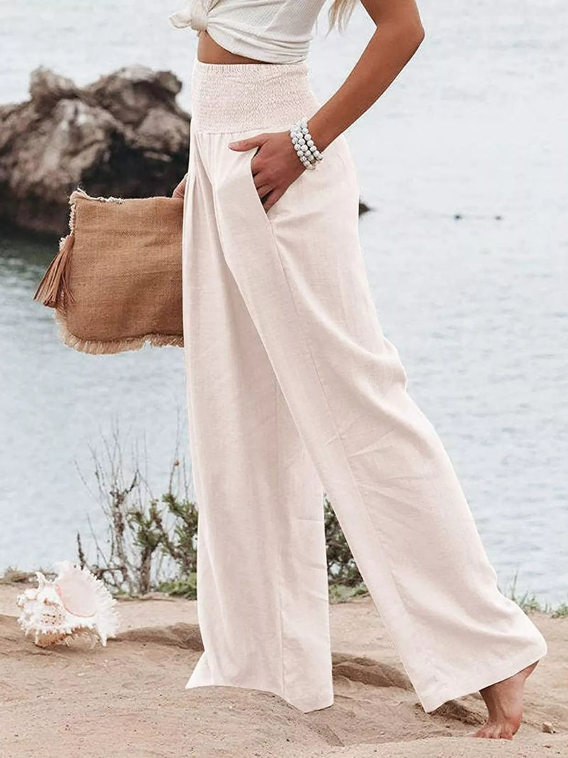 Person wearing white pants and a beige bag by a body of water.