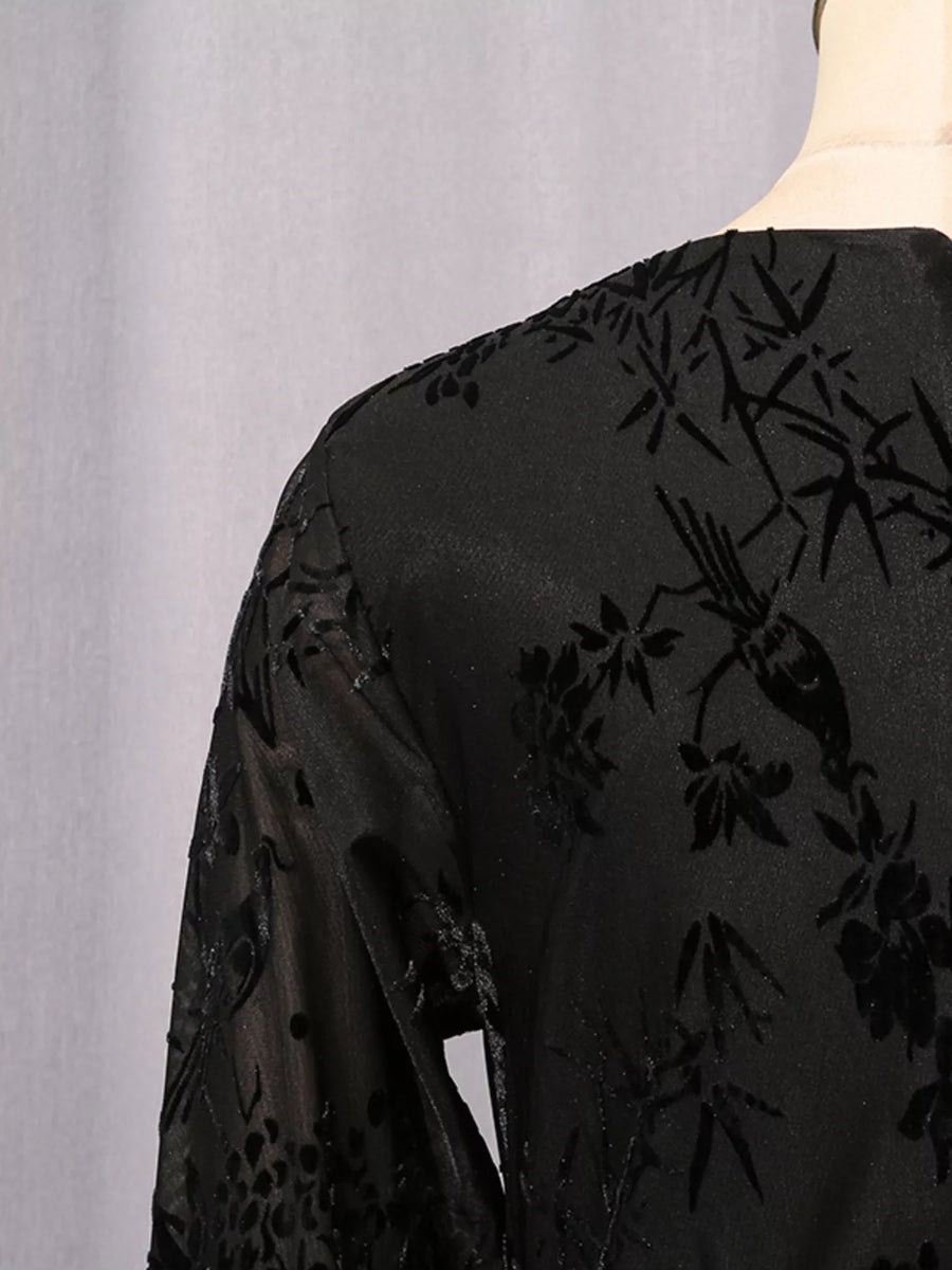 Close-up of the back of a black sheer embroidered blouse or dress with floral and bird motifs, shown on a mannequin against a light gray backdrop.