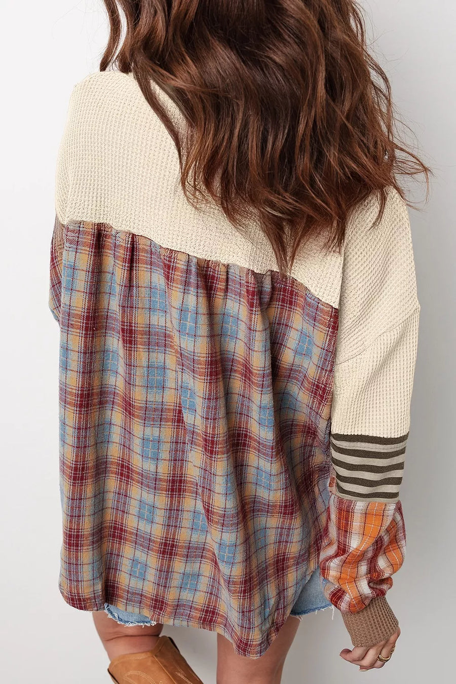 Person wearing a plaid shirt over a cream sweater with a white background