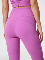 Person wearing bright purple leggings and top on a light gray background