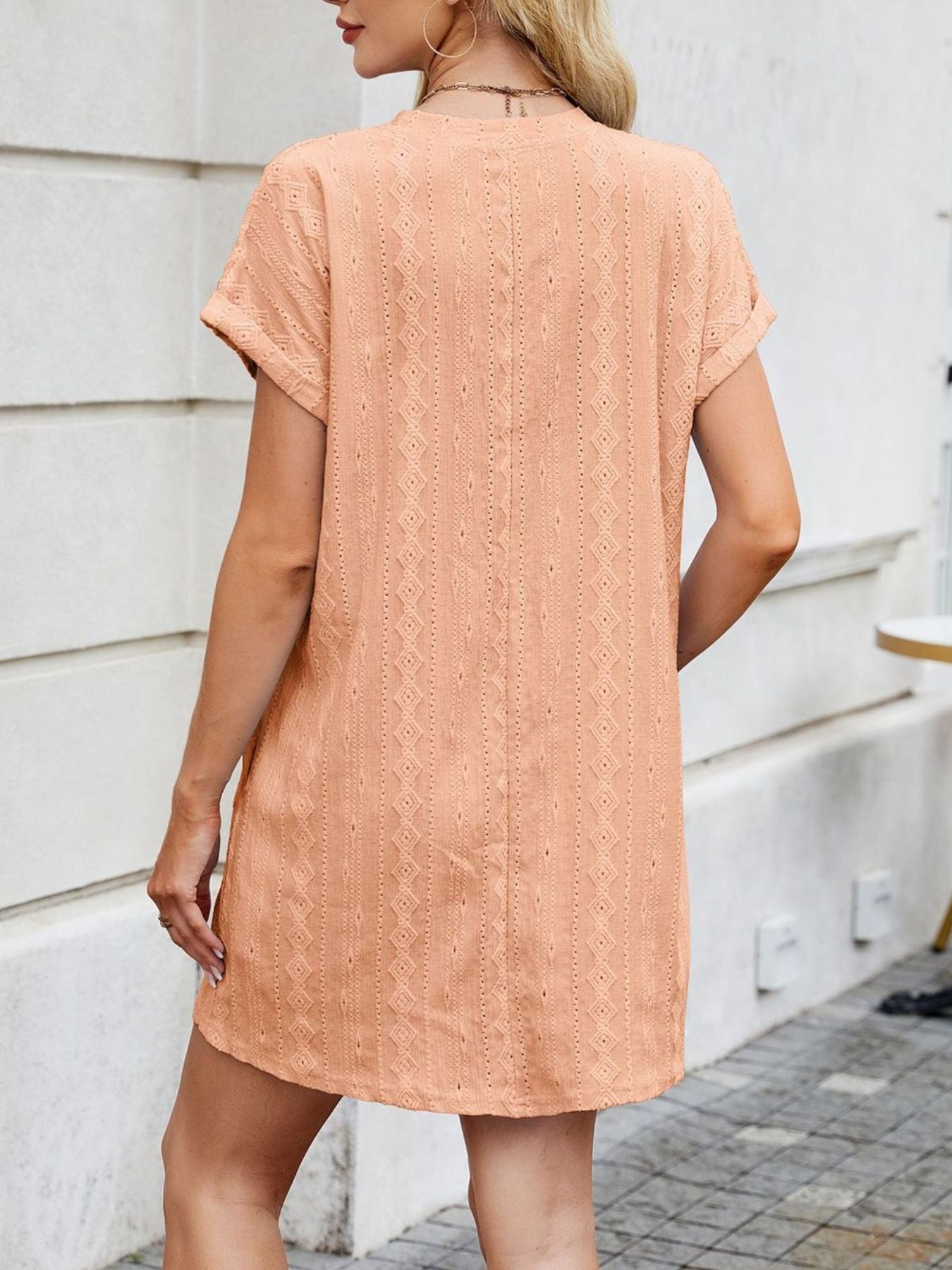Woman wearing a peach-colored lace dress standing against a light-colored wall.