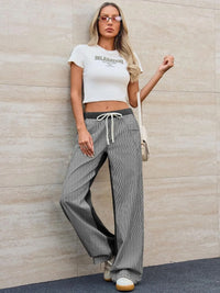 Woman wearing a white crop top and gray wide-leg pants against a beige wall.