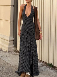 Woman wearing a black patterned dress with a brown jacket against a beige wall.