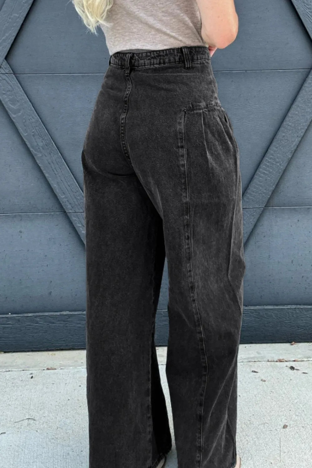 Person wearing black high-waisted pants against a blue geometric-patterned wall.