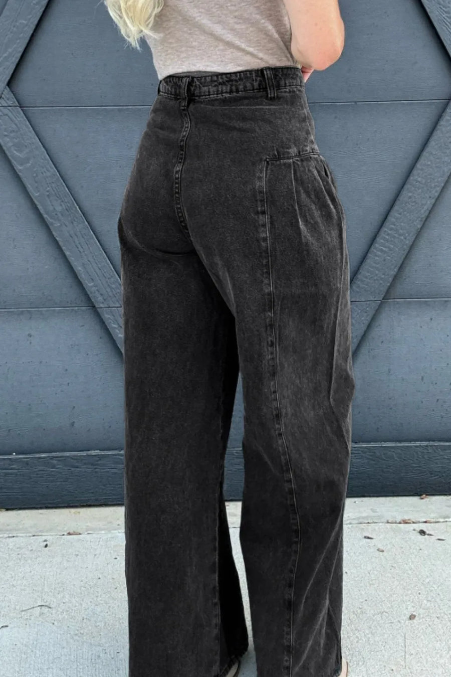 Person wearing black high-waisted pants against a blue geometric-patterned wall.
