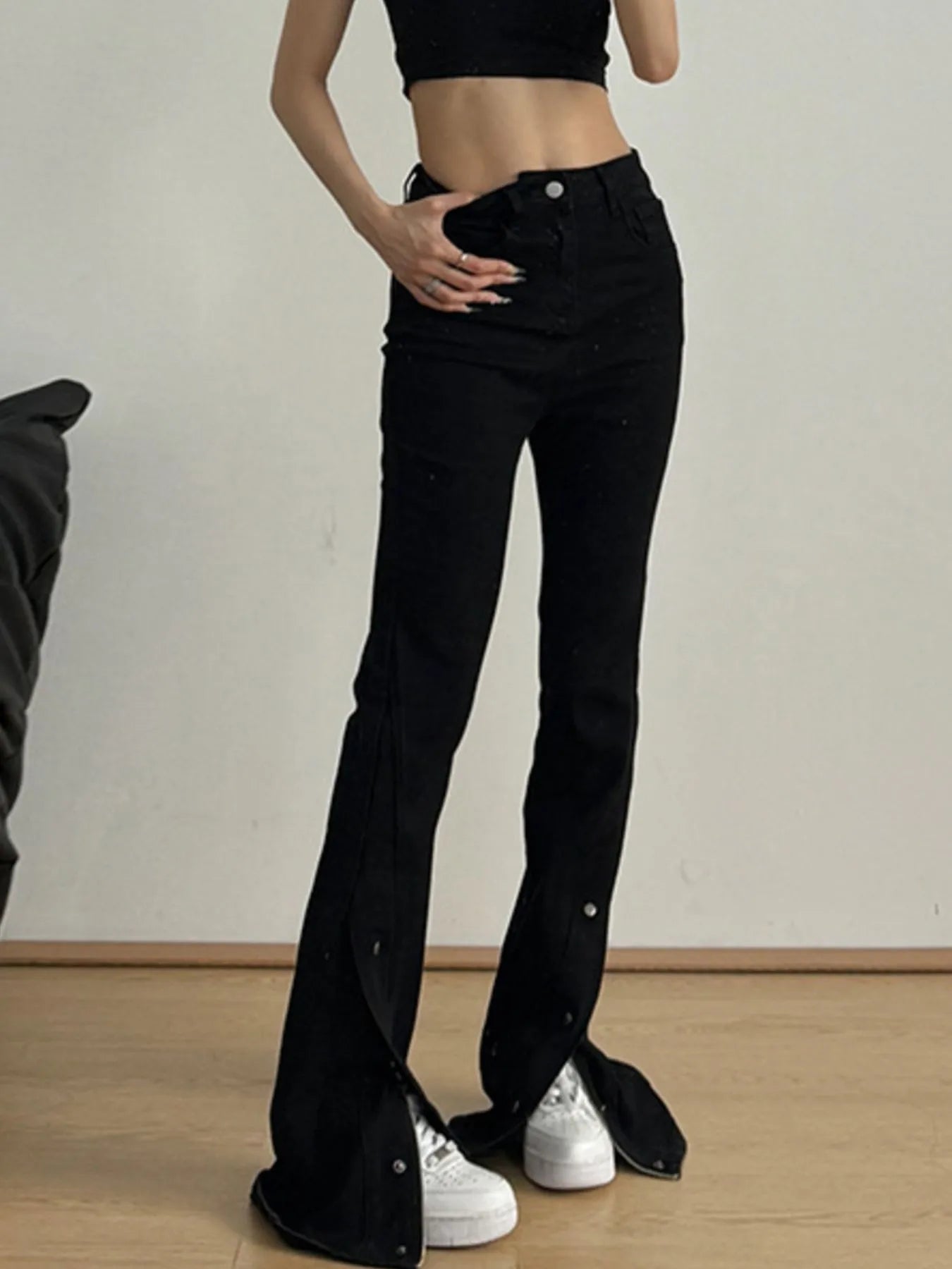 Person wearing black flared jeans and a black crop top on a plain background