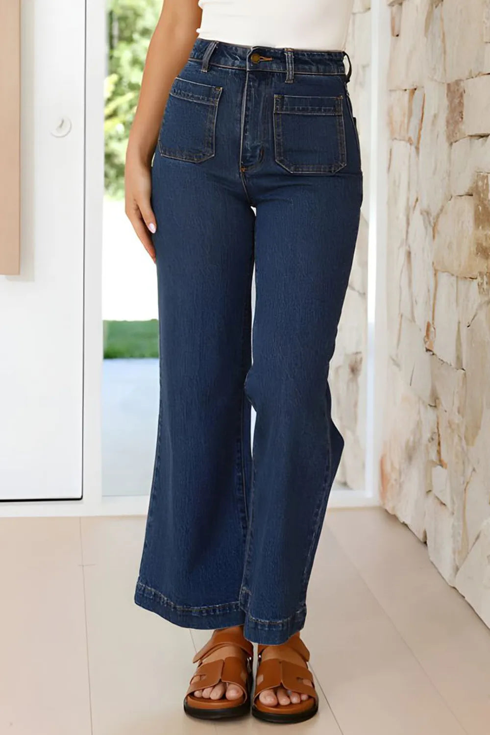 Person wearing blue jeans standing indoors with a stone wall background