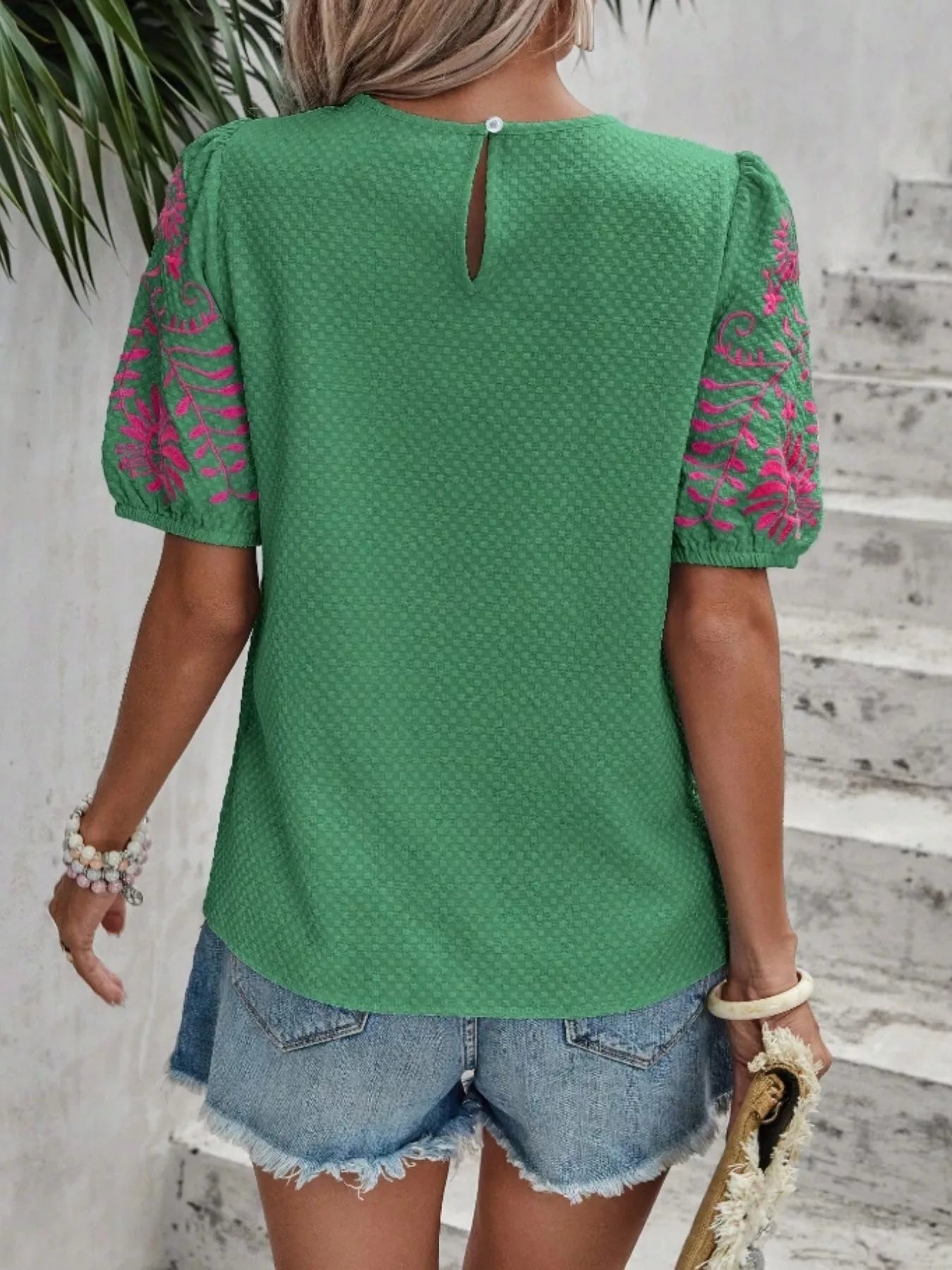Person wearing a green top with pink lace sleeves against a gray wall.