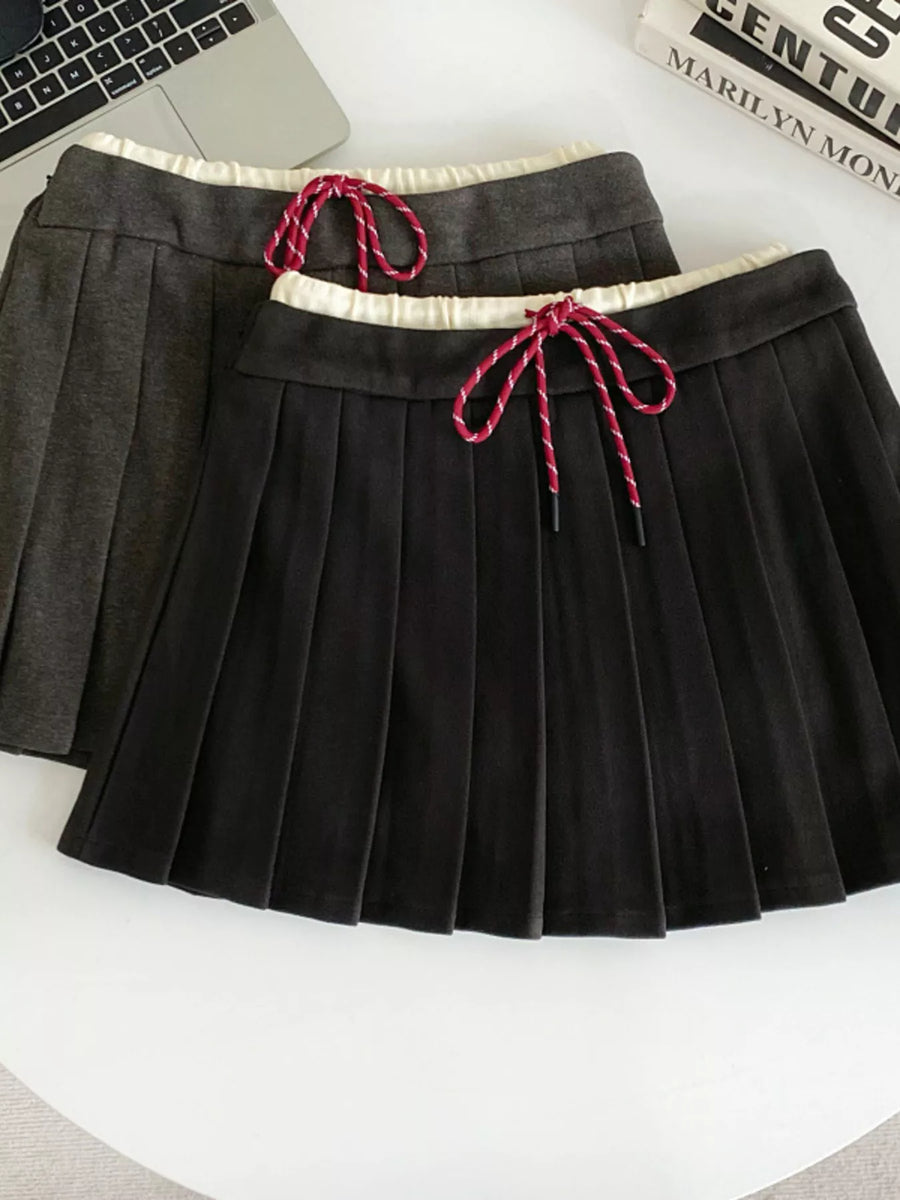 Black pleated skirt with red drawstrings on a white surface
