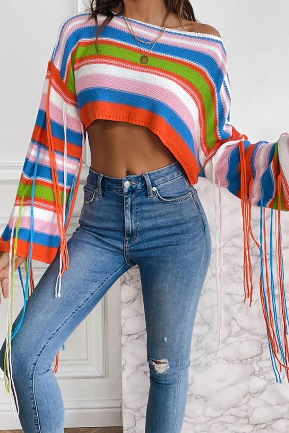 Person wearing a colorful striped sweater and blue jeans against a white wall.