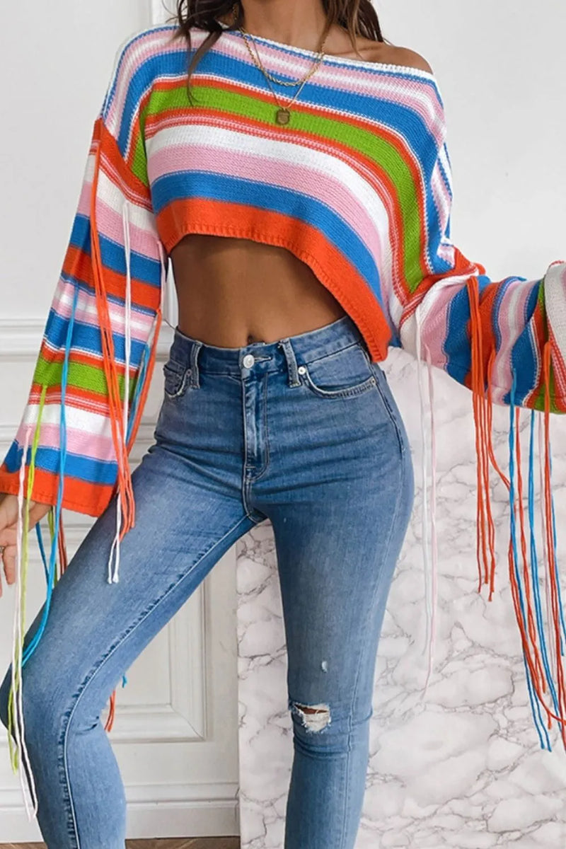 Person wearing a colorful striped sweater and blue jeans against a white wall.