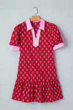 Red dress with floral pattern and pink collar on a hanger against a light gray background