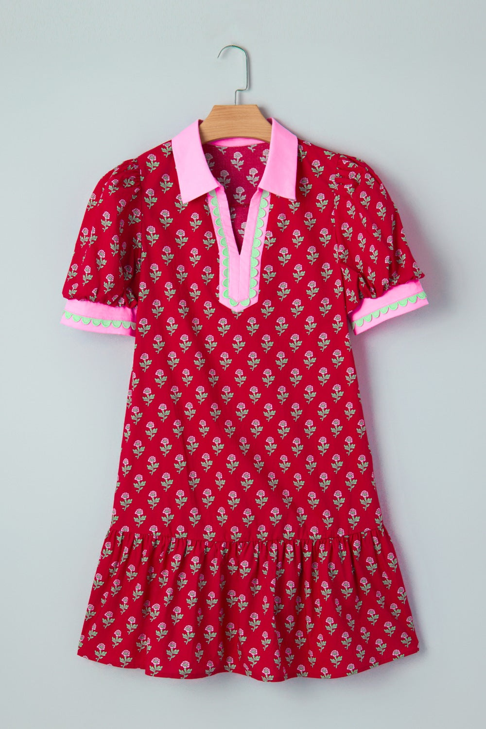Red dress with floral pattern and pink collar on a hanger against a light gray background