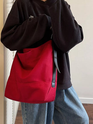 Person wearing a black hoodie and blue jeans with a red bag over one shoulder.